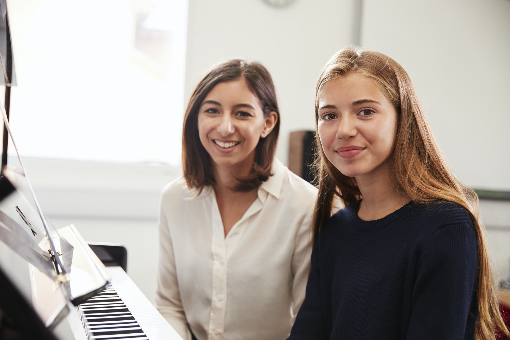 Portrait Of Pupil With Teacher Playing Piano In Music Lesson