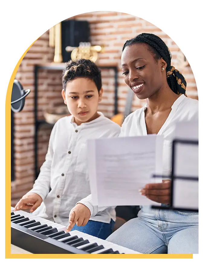 A woman and a child sit together at a keyboard piano. The woman holds sheet music and smiles as the child points at the keys, enjoying music lessons Westchase style in their cozy room.