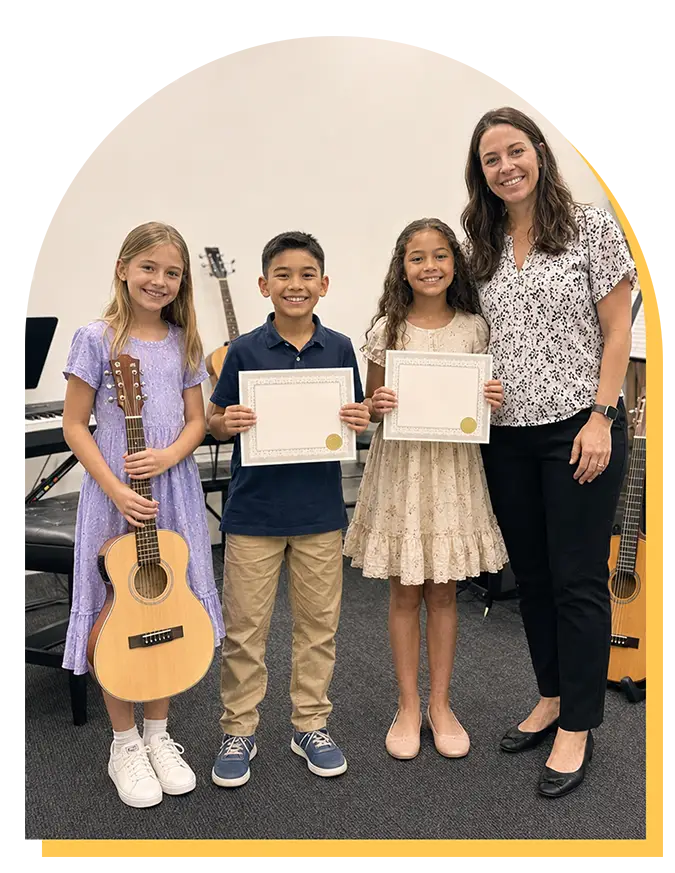 Three smiling children stand with certificates and a guitar, next to an adult woman in a music school setting. Musical instruments in the background suggest they’ve just finished music lessons Citrus Park or an award event in music lessons Tampa.